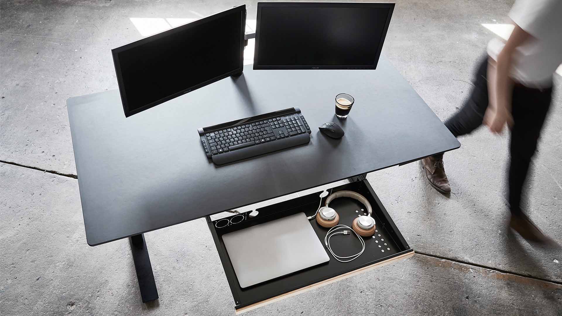 Industriele omgeving met een zwart bureau met monitoren en zwarte accesoires en een zwarte lade van PJ Production