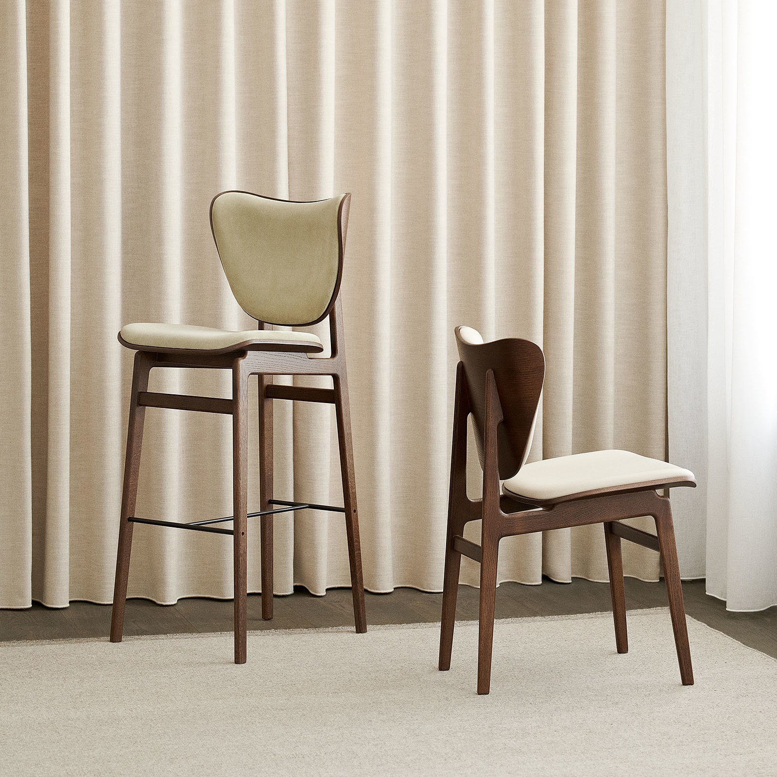 Een hoge en een lage stoel van hout voor een gordijn in neutrale kleurtinten
