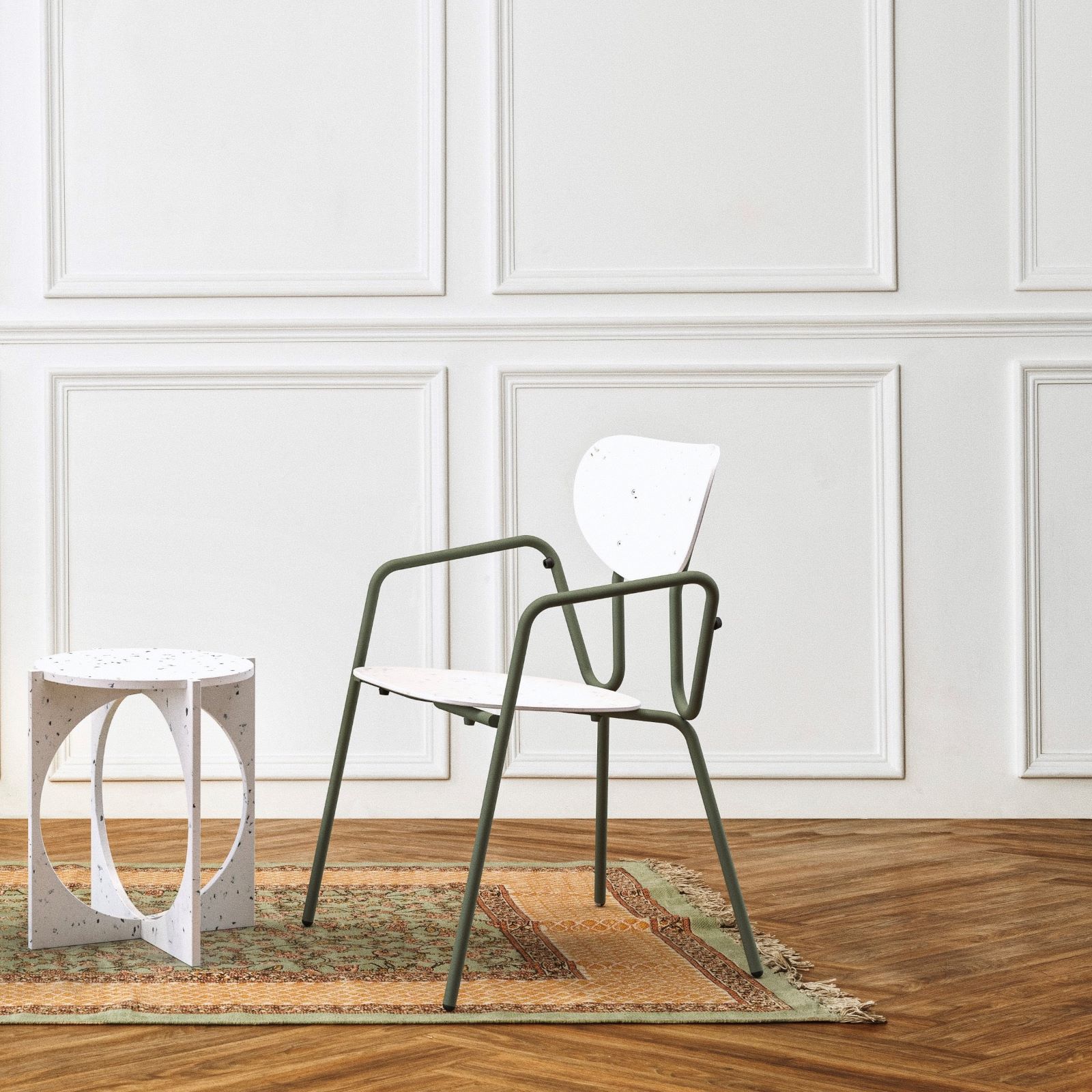 Productfoto van de stoel Kyrielle in een lege witte ruimte met een vloerkleed en kleine bijzettafeltje.