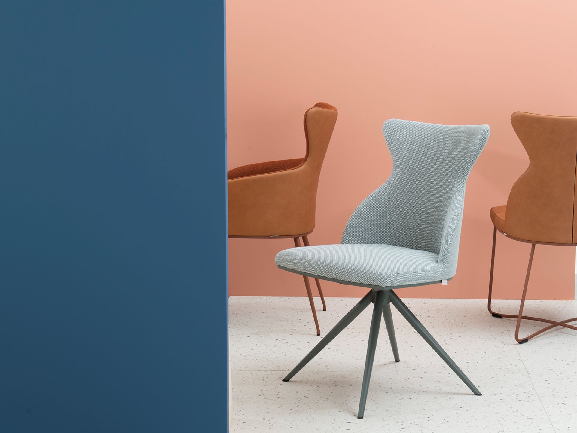 luxe blauwe stoel met grijs-zwarte poten en op de achtergrond nog twee bruine leren stoelen.