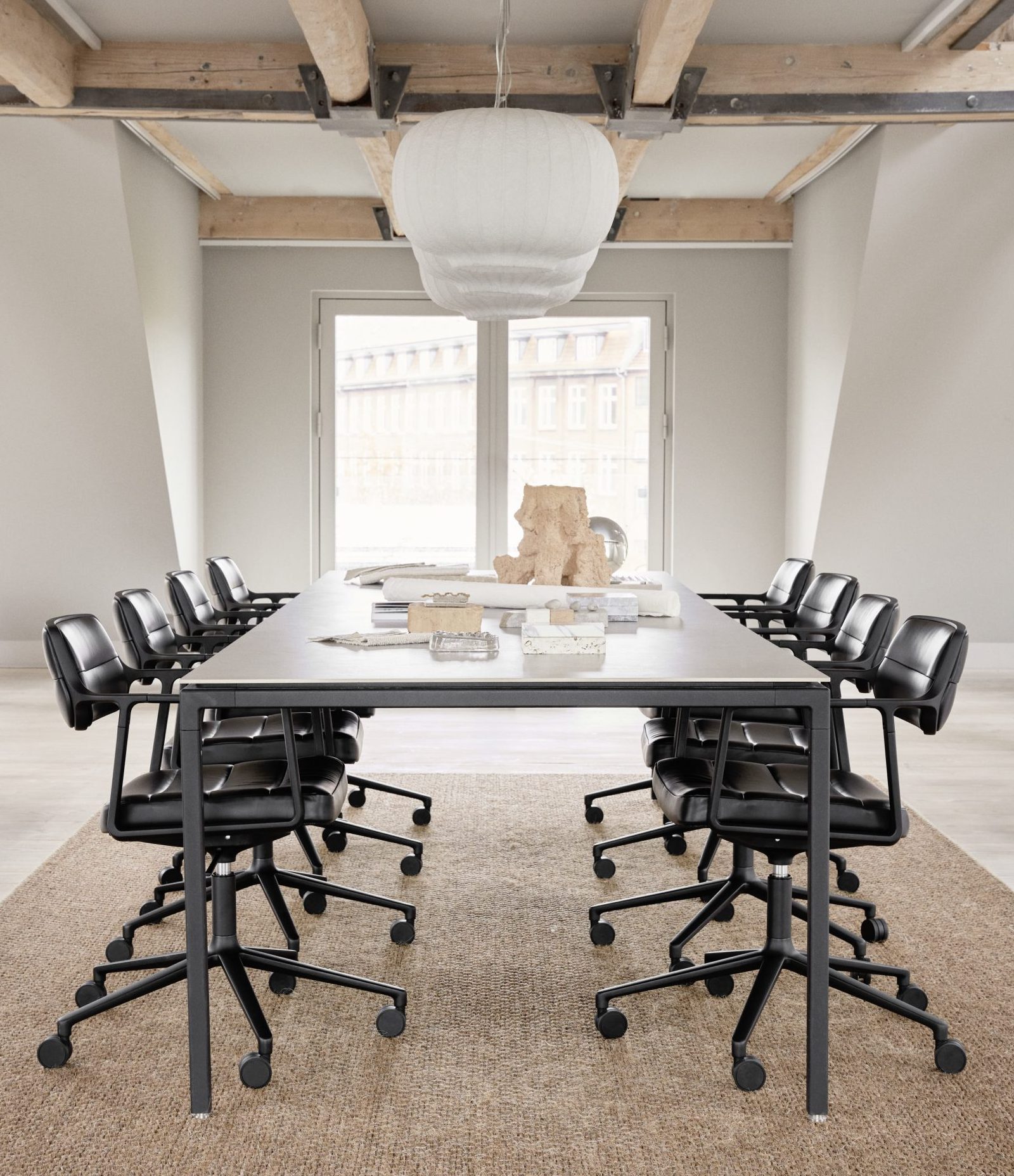 Zijaanzicht van een witte ruimte met industriële houten balken op het plafond. Midden in de kamer is een lange vergadertafel met stoelen van Vipp A/S.