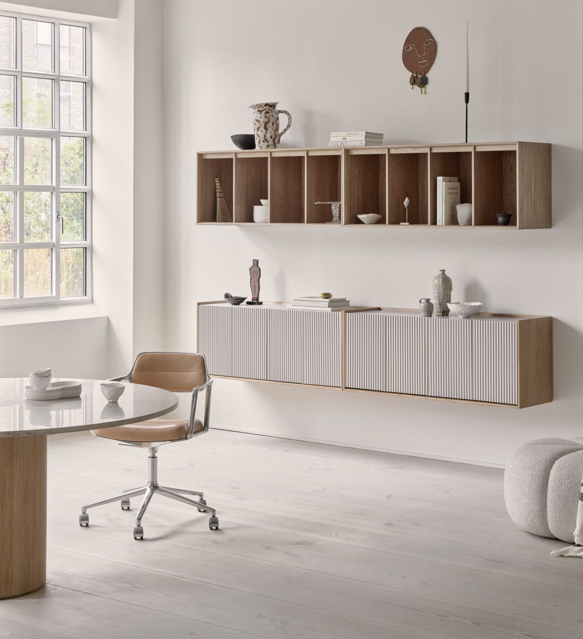 Witte kantoorruimte met ronde tafel en planken aan de muur gemaakt van licht hout.