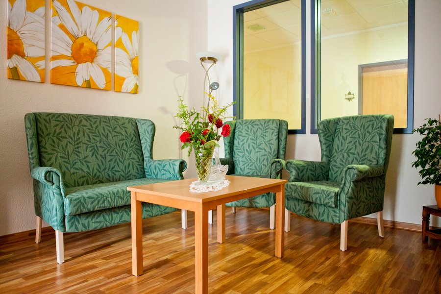 Vooraanzicht van een woonkamer met twee groene stoelen en een bank met een bijzettafel met bloemen.