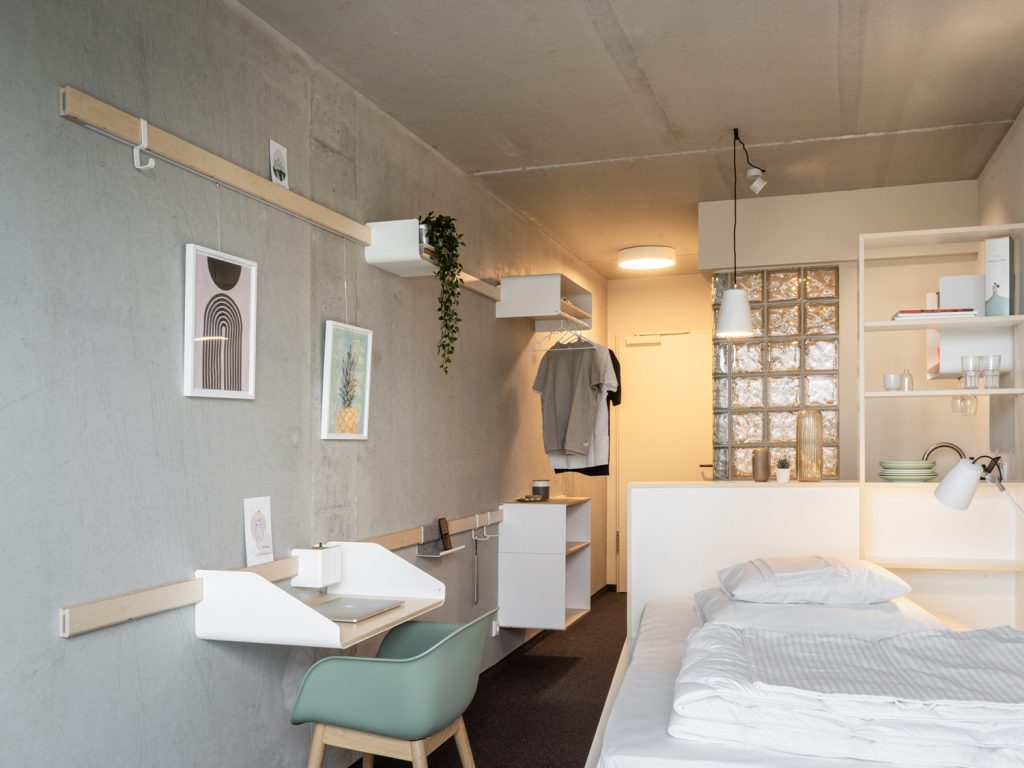 Zijaanzicht van een hotelkamer met een modulaire muursysteem met een bureau, plantenbak en kastje