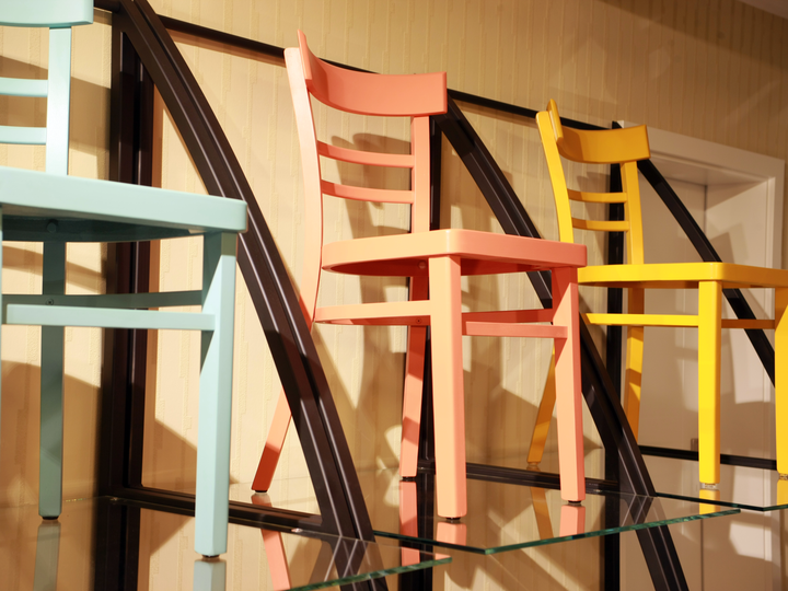 Drie dezelfde stoelen in een showroom in verschillende kleuren, lichtblauw, roze en geel.