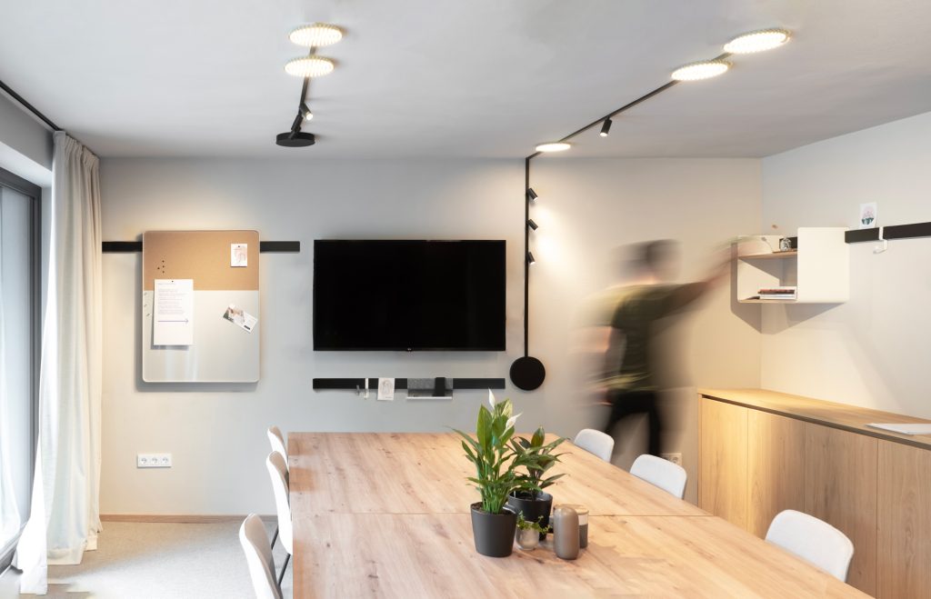 Zijaanzicht van een grote vergaderruimte met lange tafel en stoelen en wandrek van Variand.