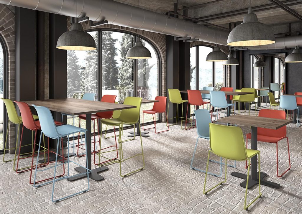 Grijze ruimte met ronde ramen en tafels en stoelen in groen, rood en blauw.
