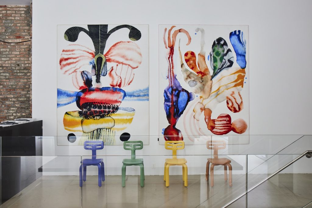Witte ruimte met abstracte schilderijen en kleurrijke stoelen.