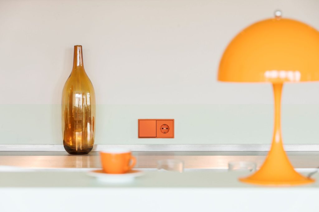 Witte keuken met oranje lamp, fles, kopje en schakelaar van Albrecht JUNG