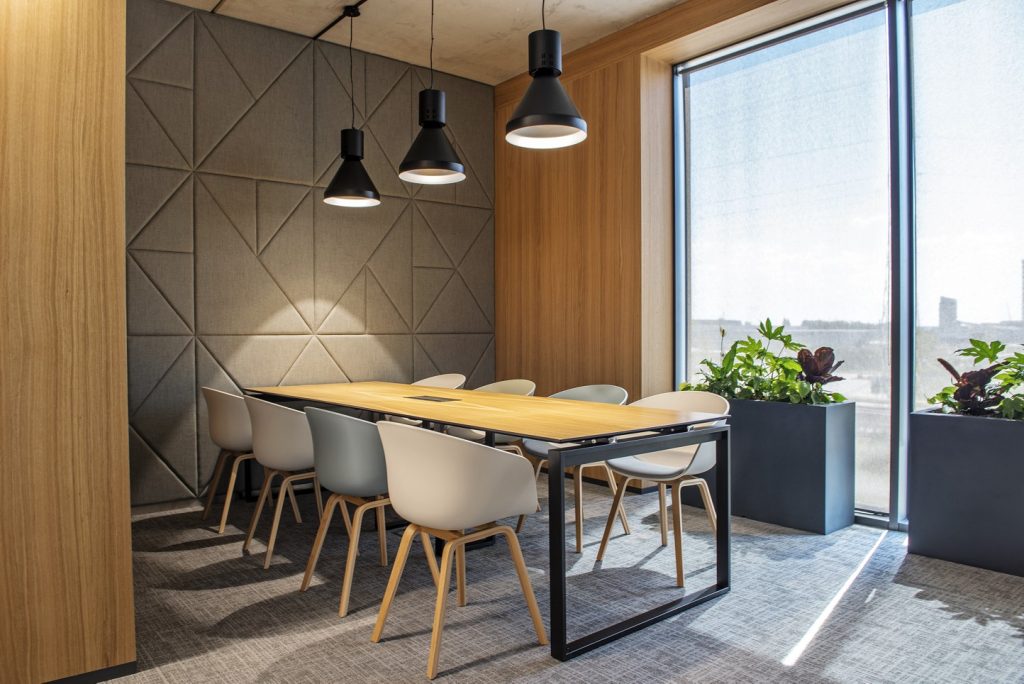Kantoorruimte met grijze geometrische muur, lange tafel met stoelen en uitzicht