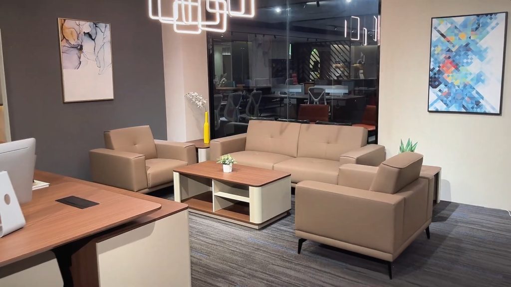 Kantoor zithoek met grote bruine bank, twee bruine stoelen en beige koffietafel.