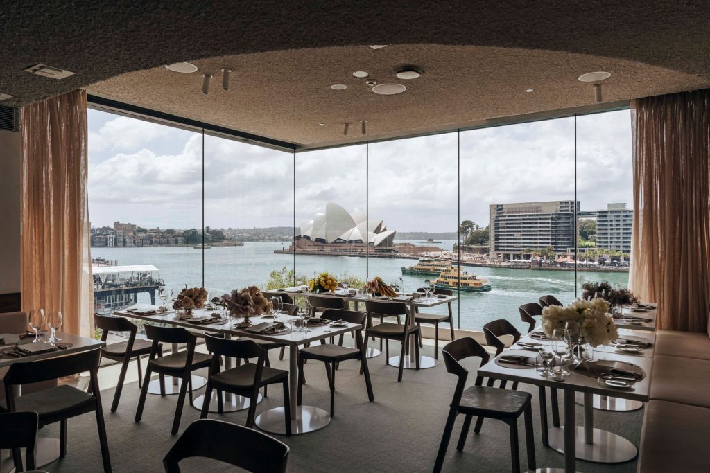 Een grote ruimte vol glazen wanden met uitzicht op de haven van Sydney met daarvoor tafels en stoelen van fabrikant Ton.
