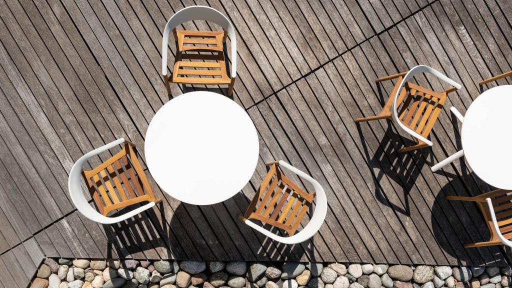 Bovenaanzicht van ronde witte tafel buiten op een terras met hout en metalen stoelen van PLANK.