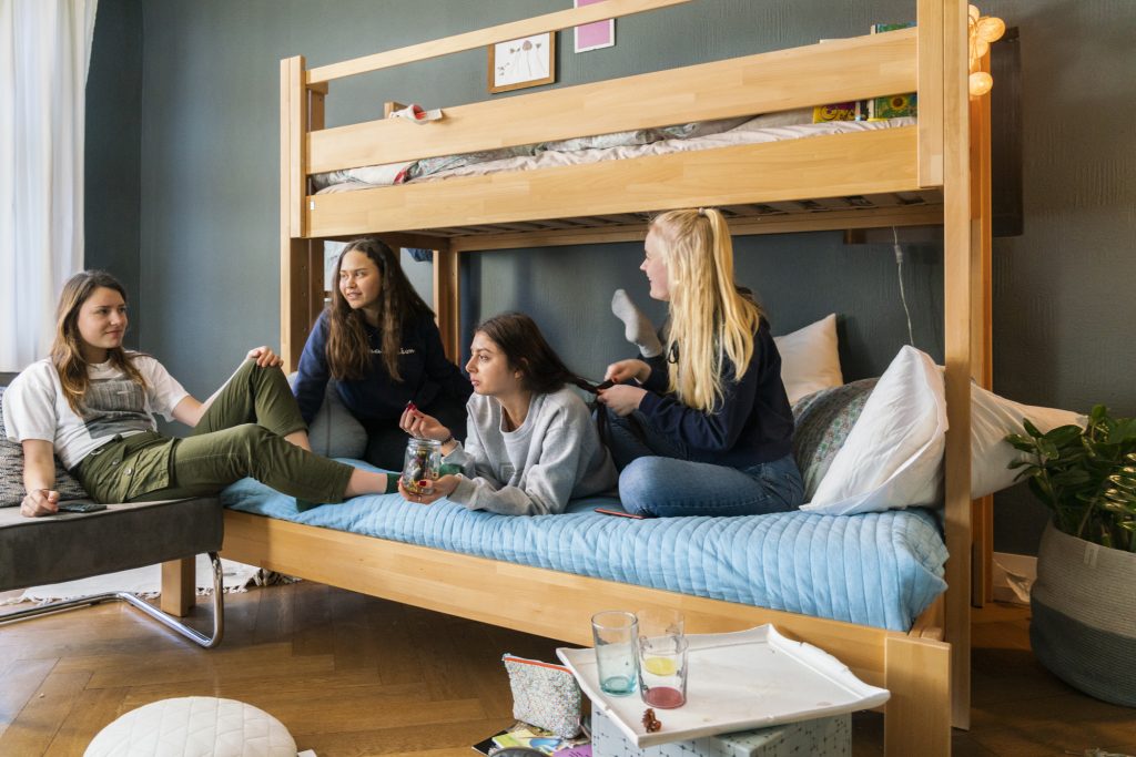 Zijaanzicht van een houten stapelbed met op de onderste bed 3 tienermeiden.