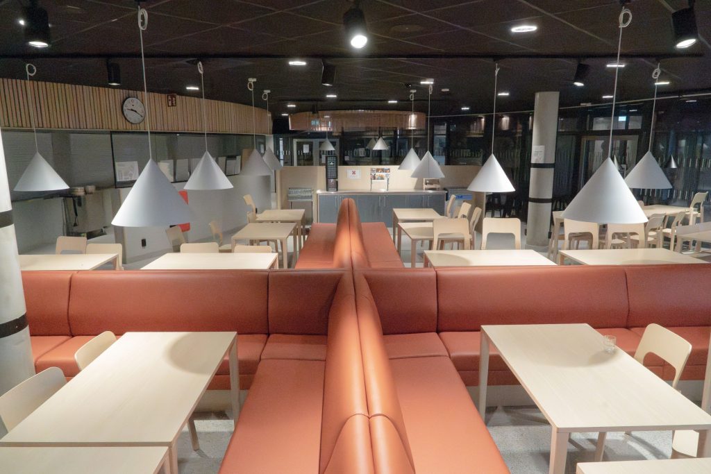 Bedrijfskantine met lange witte tafels en zalmroze leren banken van Vilax AB