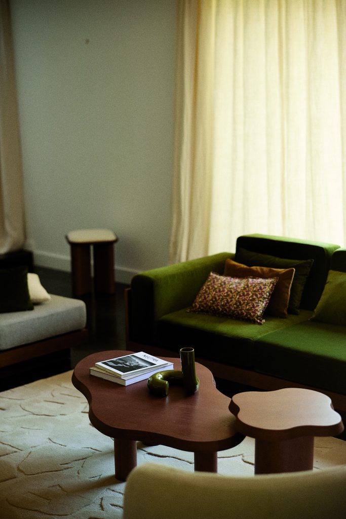 Een woonkamer met een groene bank en twee kleine organisch vormige tafeltjes.