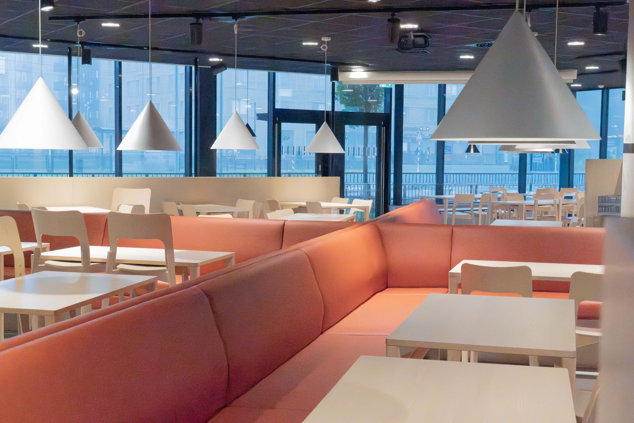Zijaanzicht van een kantine met lange witte tafels en zalmroze leren banken