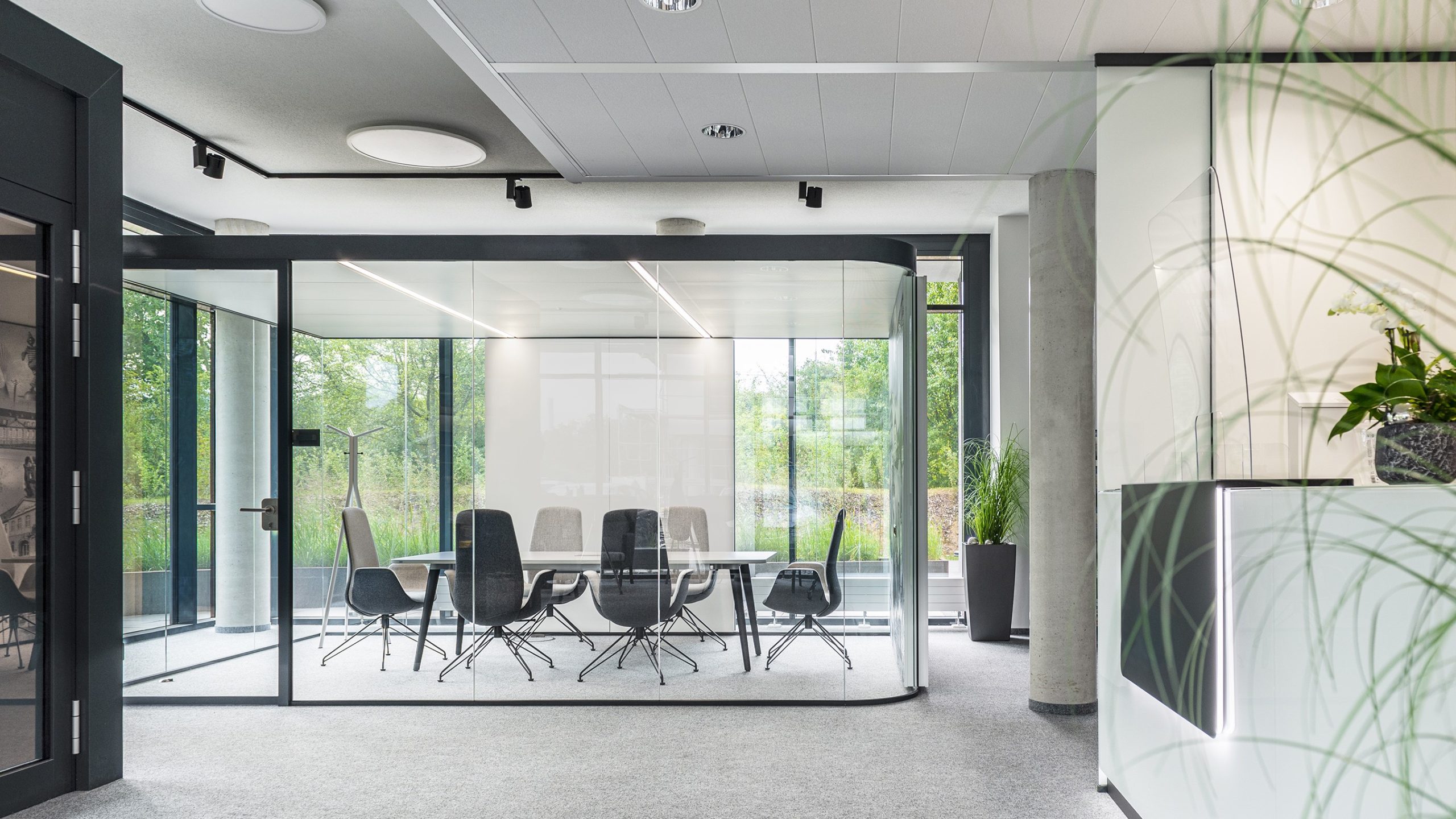 Witte kantoorruimte met zwart glazen ruimtes en tafel met stoelen.