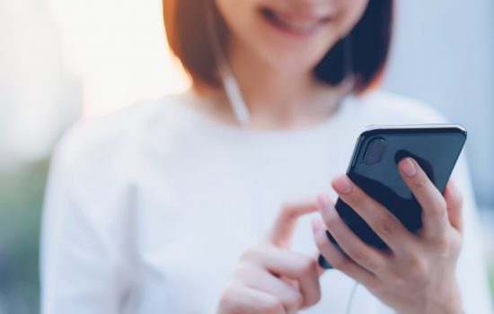 Smiling Asian woman using smartphone with listening to music and standing in office building.